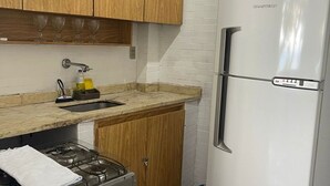 A compact kitchen with wooden cabinets, a stainless steel refrigerator, a gas stove, and a sink. - Best location facing the sea in Barra  (Barra da Tijuca Rio de Janeiro)
