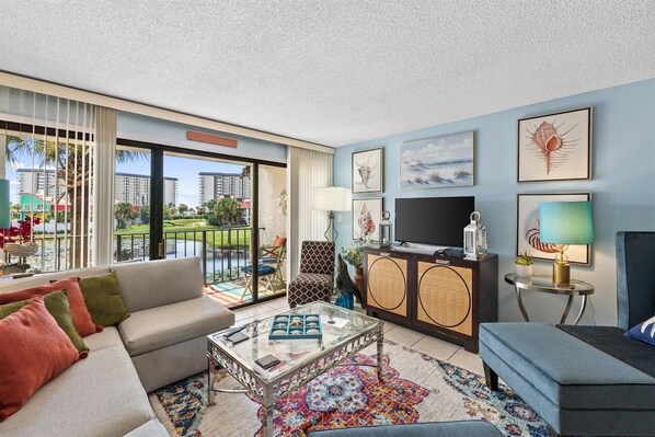 A modern living room with a sofa, armchair, and coffee table, a television, and artwork on the walls.