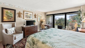 Een hotelkamer met een groot bed, een bureau met een computer, een stoel, een televisie en een balkon met uitzicht op palmbomen.