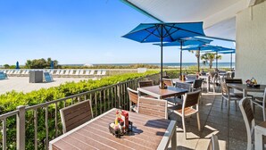 Une terrasse extérieure avec des tables et des chaises, des parasols bleus et une vue sur la plage.