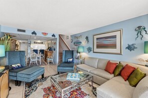 A living room with a sofa, armchairs, a coffee table, and a rug. There are wall decorations including a framed picture and wall art.