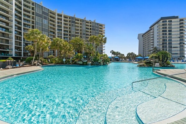 A hotel with a large swimming pool surrounded by palm trees and a clear blue sky.