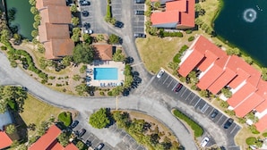 Luchtbeeld van een woonwijk met een zwembad, meerdere parkeerplaatsen en huizen met rode daken.