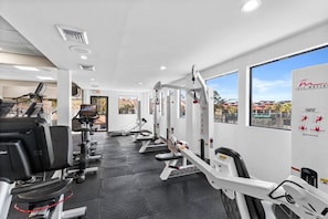 A gym with cardio machines, weight stations, and a wall-mounted poster.