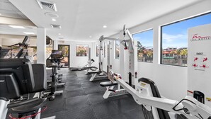 Une salle de sport équipée de machines de cardio, de postes d’entraînement avec poids et d’une grande fenêtre donnant sur des immeubles.