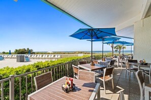A terrace with outdoor seating, a view of the beach, and a clear sky.