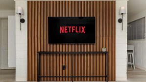 A modern living room with a large TV mounted on a wooden wall, a black console table below, and two wall-mounted lamps.
