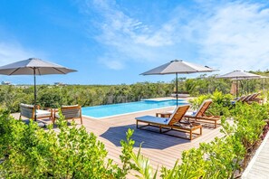 A poolside area with lounge chairs and umbrellas, surrounded by greenery.
