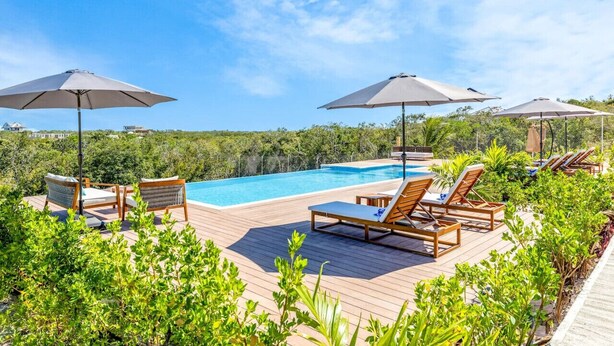 A poolside area with lounge chairs and umbrellas, surrounded by greenery.