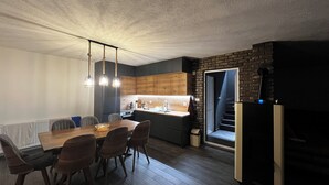 Une cuisine moderne avec des meubles en bois, un coin repas avec une table et des chaises en bois, et un escalier menant à une pièce sombre.