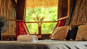A wooden bed with a dark mattress and pillows, a rolled towel, and a small table with a vase and a cup. - Bambuk Bio Chalet Uvita beach front (Uvita)