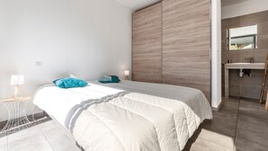 A modern bedroom with a large bed, a bedside table with a lamp, and a bathroom with a sink and mirror.