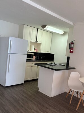 A compact kitchen with white cabinets, a white refrigerator, a black countertop, and a small island with a sink. - Ocean view with balcony private  Efficieny  atThe OceanManor (Fort Lauderdale)