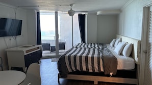 A hotel room with a bed, a desk, a TV, a balcony with a view, and a ceiling fan. - Ocean view with balcony private  Efficieny  atThe OceanManor (Fort Lauderdale)