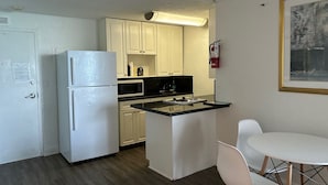 A compact kitchen with white cabinets, a refrigerator, a microwave, and a gas stove. There's a small dining area with a white table and chairs. - Ocean view with balcony private  Efficieny  atThe OceanManor (Fort Lauderdale)