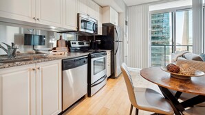 A modern kitchen with white cabinetry, stainless steel appliances, and a dining area with a wooden table and chairs. - Beautiful and Stylish 1 BR Condo in DT Toronto (Toronto)