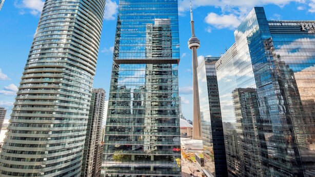 A modern cityscape with high-rise buildings, including a distinctive tower with a spire, and a prominent glass building reflecting the sky. - Beautiful and Stylish 1 BR Condo in DT Toronto (Toronto)