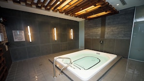 Moderni spa-huone, jossa on suuri kylpyamme, puupalkit katossa ja seinällä terveysvaroitusmerkki.