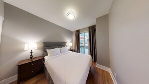 Une chambre d’hôtel avec un lit, deux tables de chevet avec des lampes, une fenêtre avec des rideaux et un luminaire au plafond.