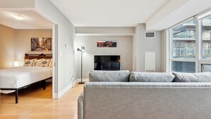 A modern living room with a sofa, a bed, a TV, and artwork on the walls. - Charming 1-BR Condo in DR Toronto (Toronto)