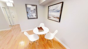 A dining area with a round white table and two white chairs, a framed abstract painting, and a framed landscape painting on the wall. - Centrally Located 1-BR Condo in DT Toronto (Toronto)