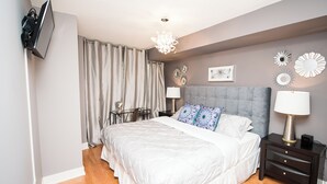 A bedroom with a bed, bedside tables, a lamp, and a TV mounted on the wall. - Charming 2-BR Condo in DR Toronto (Toronto)