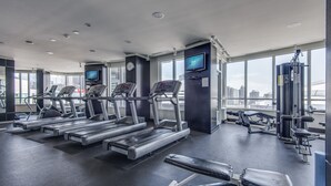 A modern gym with treadmills, weight machines, and a large window offering a city view. - Charming 2-BR Condo in DR Toronto (Toronto)