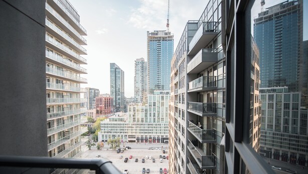 A high-rise building with multiple balconies and a view of a parking area with several cars. - Charming 2-BR Condo in DR Toronto (Toronto)