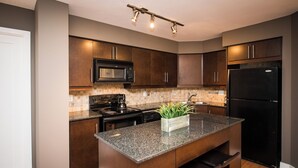 A modern kitchen with dark brown cabinets, a granite countertop, a black refrigerator, and a microwave. - Charming 2-BR Condo in DR Toronto (Toronto)