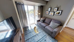 A modern living room with a grey sofa, patterned cushions, a glass coffee table, and a TV. - Charming 3-BR Condo in DR Toronto (Toronto)