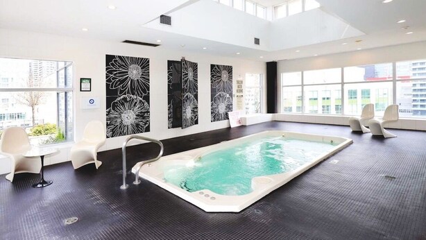 A modern indoor pool area with a large rectangular pool, white chairs, and black and white floral wall art. - Charming 3-BR Condo in DR Toronto (Toronto)