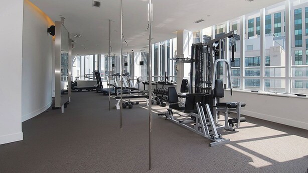 Ein modernes Fitnessstudio mit unterschiedlichen Trainingsgeräten, großen Fenstern und einem hellen, großzügigen Raum.