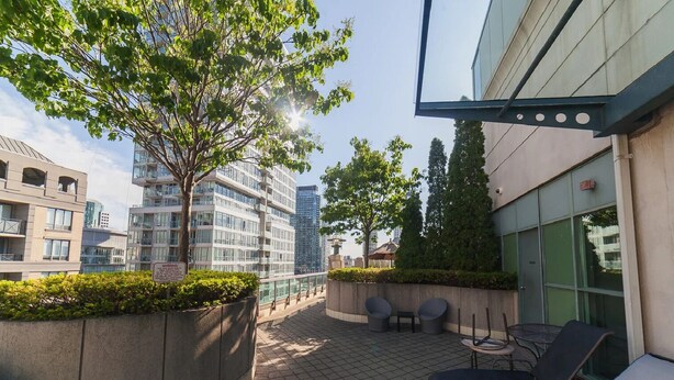 A rooftop terrace with outdoor seating, a tree, and modern buildings in the background. - Centrally Located 2-BR Condo in DT Toronto (Toronto)