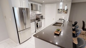 A modern kitchen with stainless steel appliances, a central island, and a dining area with chairs. - Centrally Located 2-BR Condo in DT Toronto (Toronto)