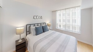 A bedroom with a bed, two bedside tables, a window with blinds, and a wall-mounted decoration. - Centrally Located 2-BR Condo in DT Toronto (Toronto)