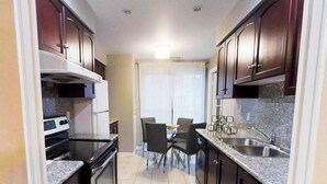 A compact kitchen with dark wooden cabinets, a built-in oven, and a dining area with a table and chairs. - Centrally Located 3-BR Condo in DT Toronto (Toronto)
