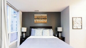 A hotel room with a large bed, two bedside tables with lamps, a window with curtains, and a wall-mounted artwork. - Centrally Located 3-BR Condo in DT Toronto (Toronto)