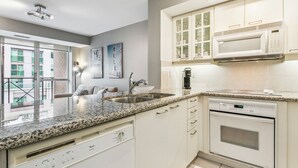 A modern kitchen with granite countertops, white cabinetry, a built-in microwave, and a dishwasher. - Modern 1-BR Condo DT Toronto (Toronto)