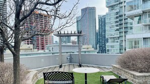 Ein Dachgarten mit einer Pergola, einer Sitzgelegenheit und Blick auf hohe Gebäude.