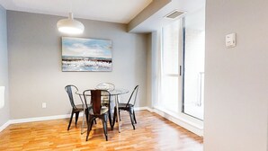 Ein Essbereich mit einem runden Tisch, vier Stühlen, einer Pendelleuchte und einem Strandbild an der Wand.