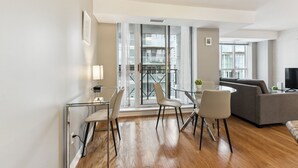 A modern living room with a glass dining table, grey sofa, and wooden flooring. - Modern 1+1-BR Condo DT Toronto (Toronto)