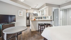 Une chambre d’hôtel compacte comprenant un coin cuisine, un espace repas avec une table et des chaises, un lit et un téléviseur.