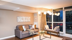 A modern living room with a grey sofa, a glass coffee table, and a city view through large windows. - Amazingly Spacious 2-BR Condo in DT Toronto (Toronto)