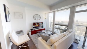 A modern living room with a white sofa, a glass coffee table, and a red entertainment unit with a television. - Fully-Equipped 3-BR Condo in DT Toronto (Toronto)