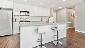 Une cuisine moderne avec des meubles blancs, des appareils en acier inoxydable et un îlot central doté de tabourets de bar.