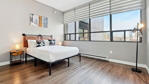 Une chambre à coucher moderne avec une grande fenêtre, un lit, une table de chevet et une lampe sur pied.