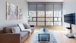 A modern living room with a sofa, a coffee table, a TV, and large windows with blinds. - Lovely 1-BR in DT Toronto (Toronto)