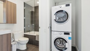 A compact bathroom with a toilet, a glass-enclosed shower, and a stacked washer and dryer. - Lovely 1-BR in DT Toronto (Toronto)