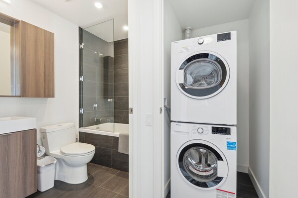 A compact bathroom with a toilet, a glass-enclosed shower, and a stacked washer and dryer. - Lovely 1-BR in DT Toronto (Toronto)
