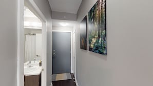 A hallway with a bathroom on the left, a door at the end, and two forest-themed paintings on the right wall. - Modern Central 1-BR Condo in DT Toronto (Toronto)